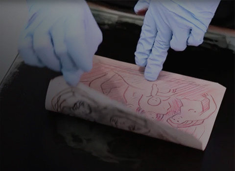 Gloved hands peeling off a print from an experimental replication of a monotype printing technique