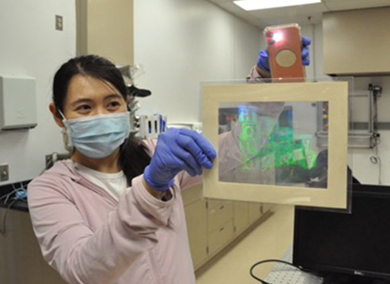 Researcher holds up a hologram, illuminated easily with the light from a phone's camera.